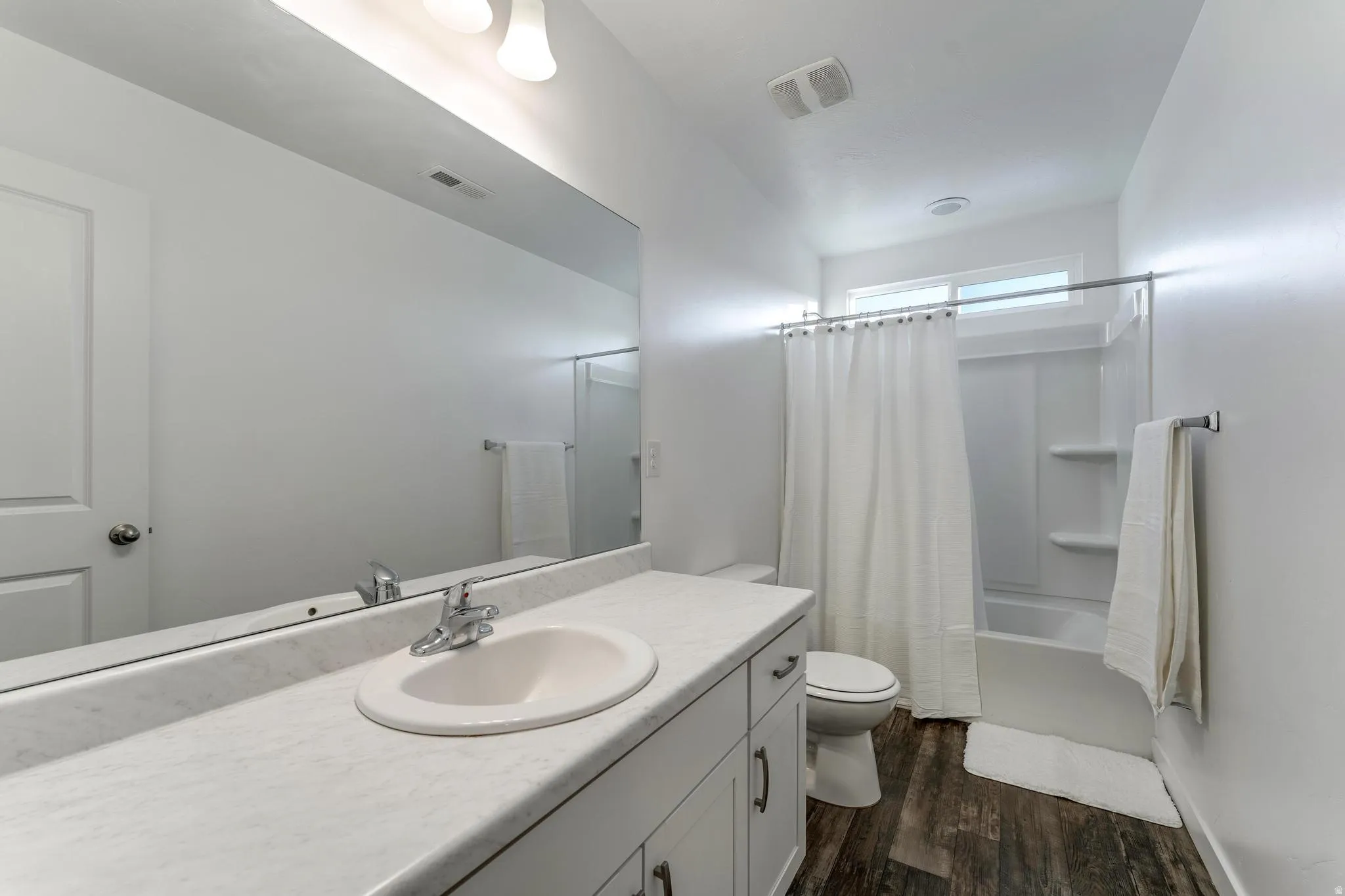 Bathroom featuring a single vanity with an integrated sink, a large wall-mounted mirror, and wood-finish flooring
