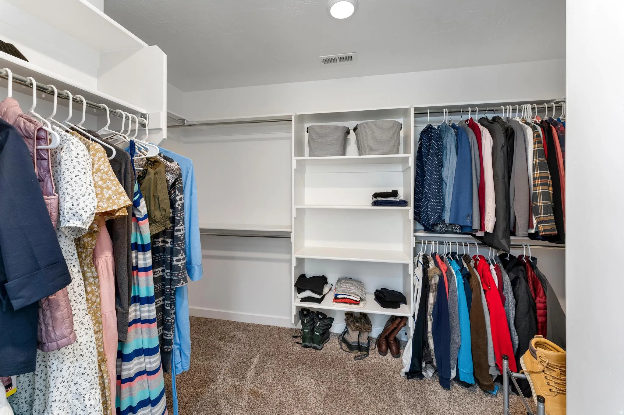 Spacious walk-in closet featuring white built-in shelving, multiple hanging rods, and neutral-toned carpeting