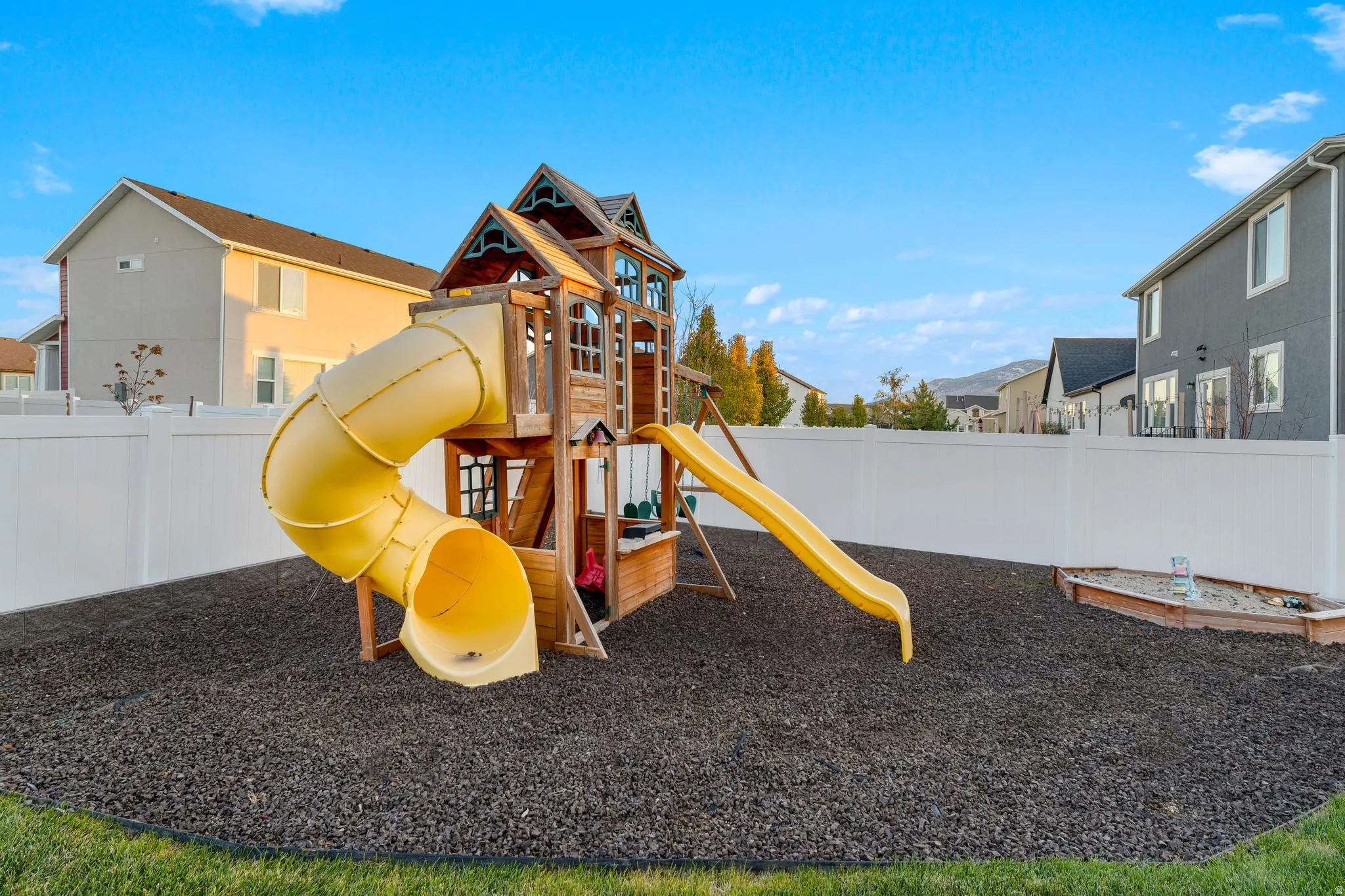 Rear yard with a white privacy fence, featuring a wooden playset with a yellow tube slide and a yellow open slide