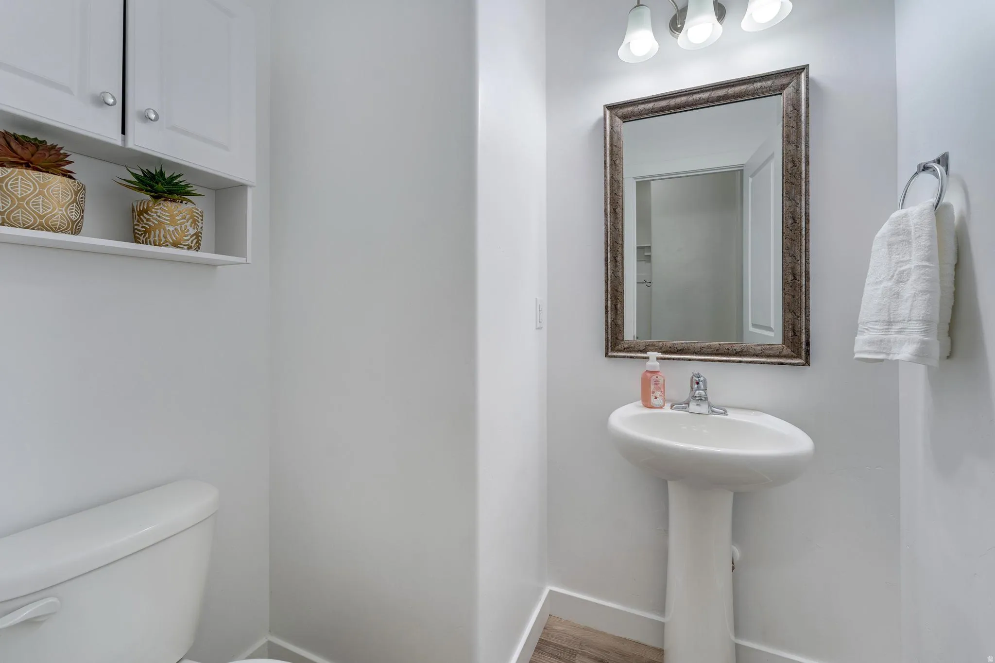 Pedestal sink with chrome faucet, framed mirror, and three-light vanity fixture