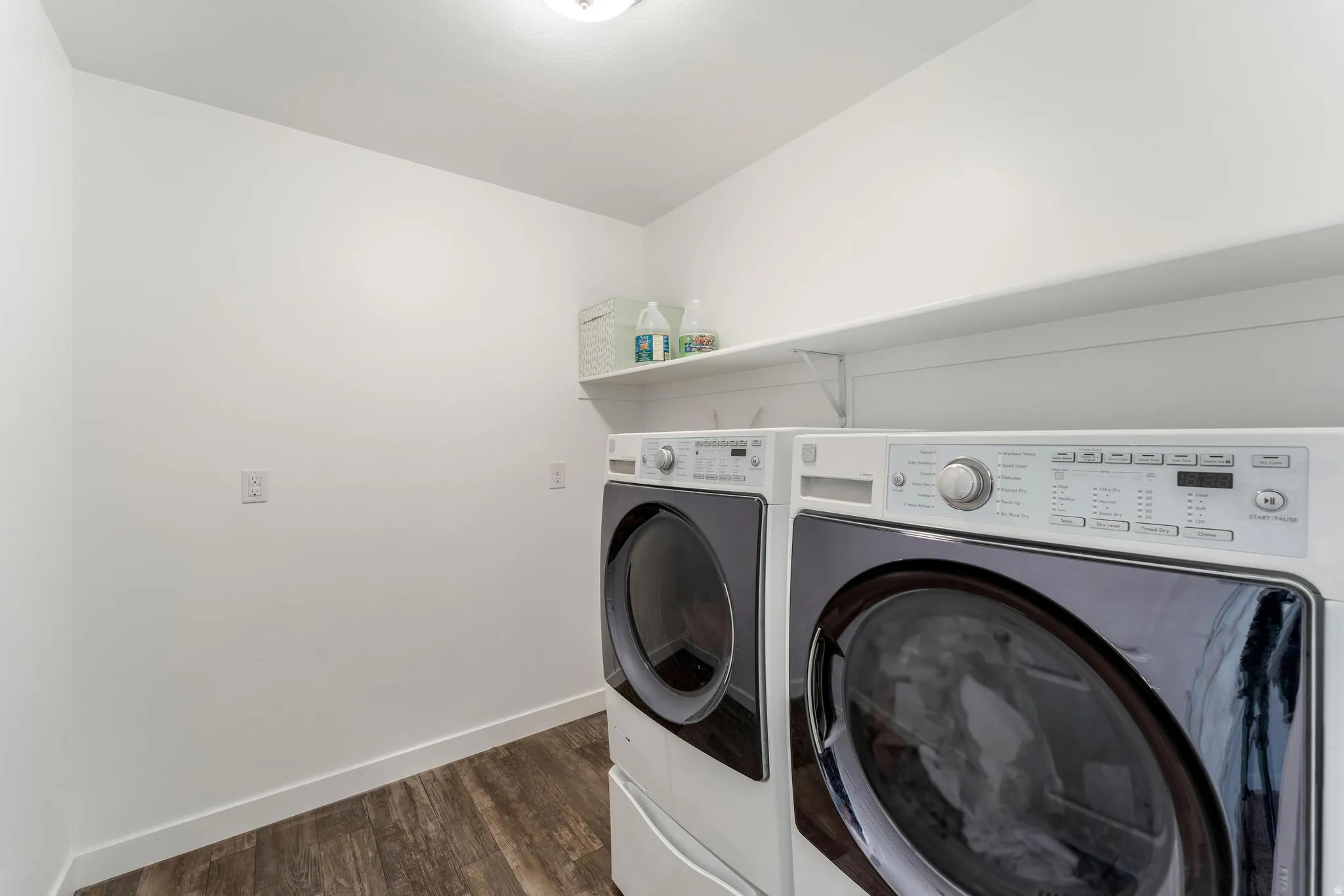 Dedicated laundry area featuring wood-finish flooring, white walls, and a convenient wall-mounted shelf