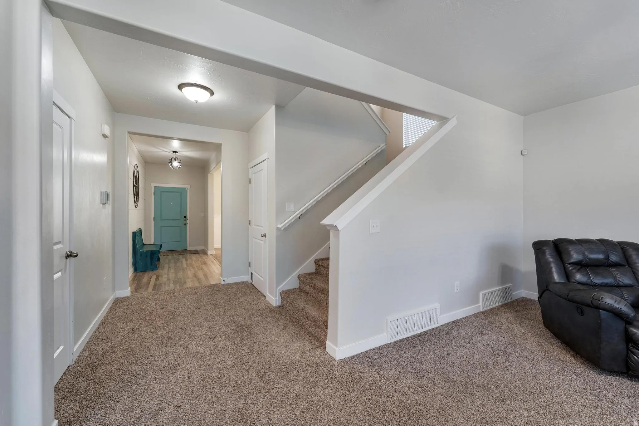 Carpeted living area featuring a staircase with white railings, a recessed entryway with wood-finish flooring, and a brightly colored entry door