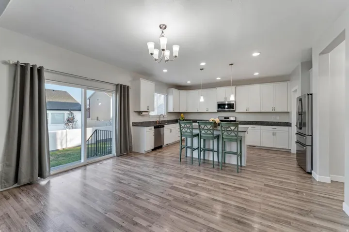 Open concept kitchen featuring white cabinetry, dark countertops, a central island with seating, stainless steel appliances, and wood-finish flooring