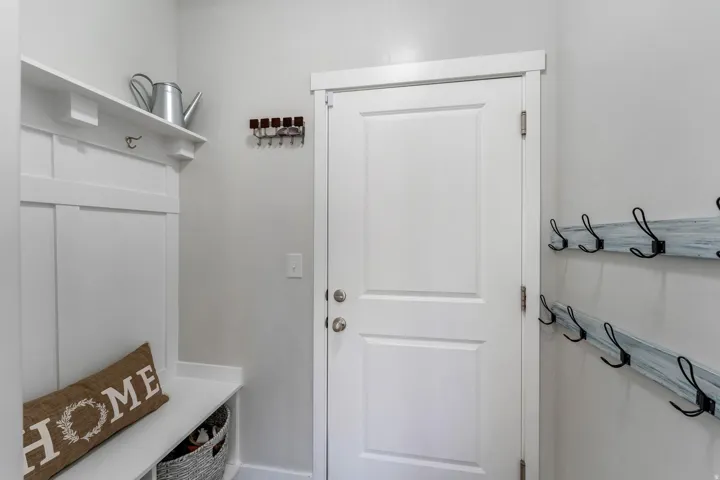 Entryway featuring a white paneled door, built-in coat rack with shelf and bench, and additional wall-mounted coat hooks