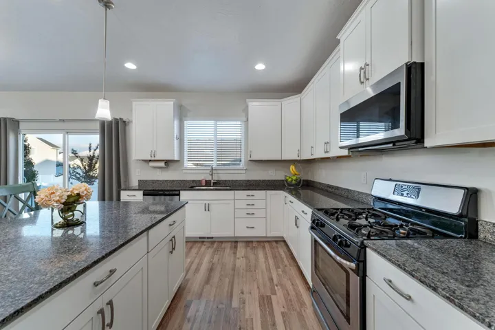 Spacious kitchen featuring white cabinetry, stone-finish countertops, wood-finish flooring, stainless steel appliances, and an island with pendant lighting