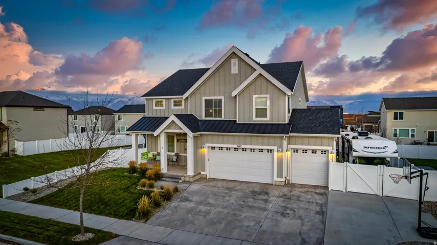 Contemporary two-story residence featuring a two-car garage, an additional single-car garage, a covered front porch, and a well-maintained front lawn with mature landscaping