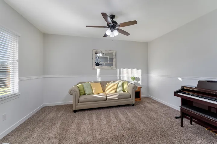 Spacious room featuring neutral paint, chair rail molding, a ceiling fan with light fixture, and plush carpet flooring