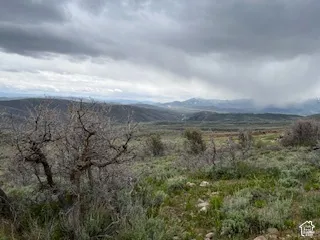 Expansive natural landscape featuring rolling hills, varied vegetation, and distant mountain ranges with snow-capped peaks