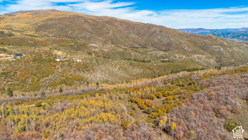 Expansive mountainous terrain featuring diverse foliage and a scattered residential structure