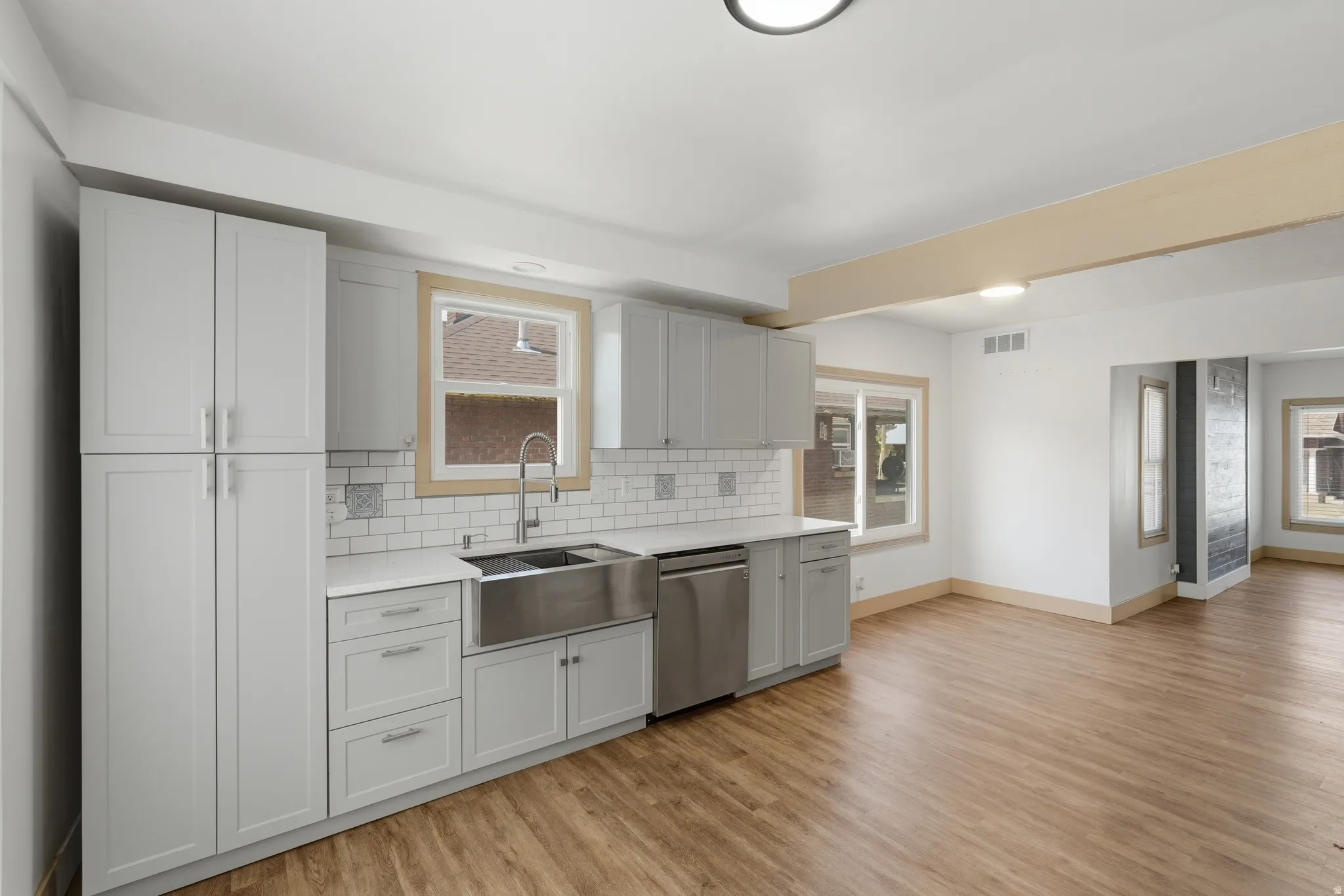 Kitchen featuring light gray cabinetry, white countertops, subway tile backsplash, a stainless steel farmhouse sink, and wood-finish flooring