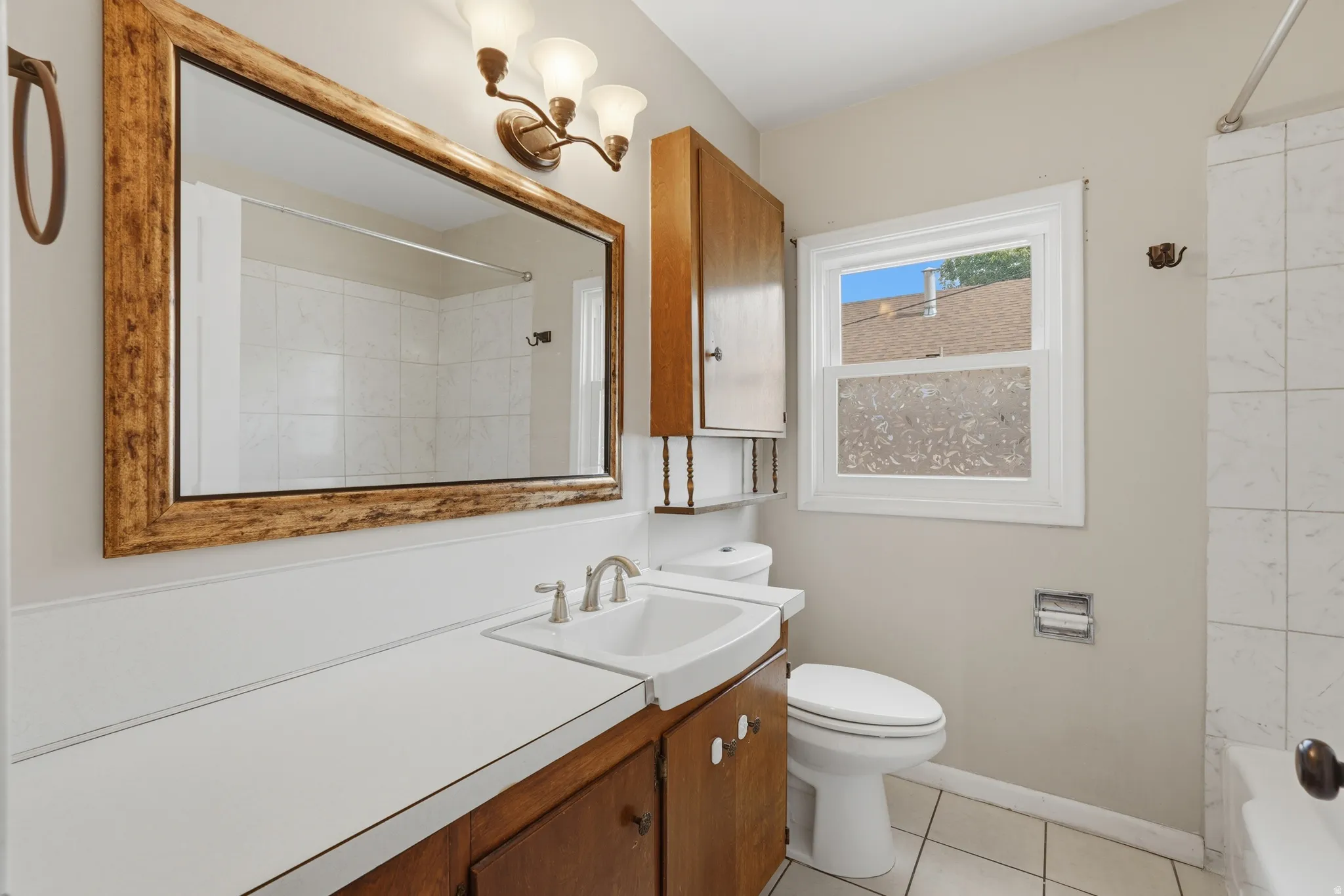 Bathroom featuring a vanity with wood-finish cabinetry and a white countertop, a rectangular mirror with a decorative frame, and a window providing natural light