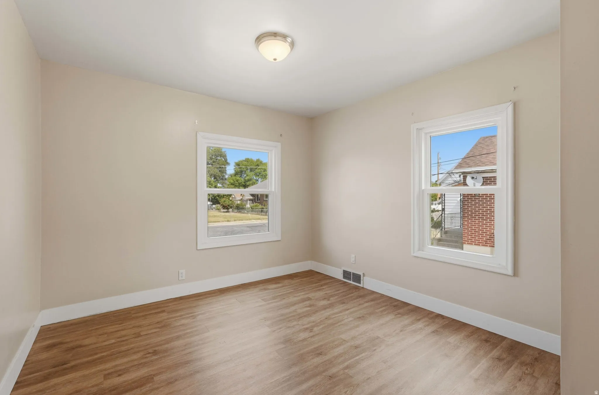 Neutral wall finishes, wood-finish flooring, white trim, and two windows