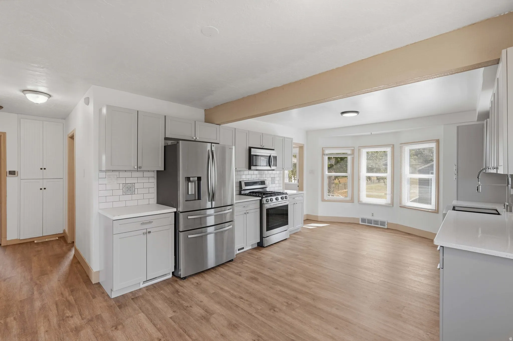 Modern kitchen featuring light gray cabinetry, stainless steel appliances, white subway tile backsplash, and wood-finish flooring