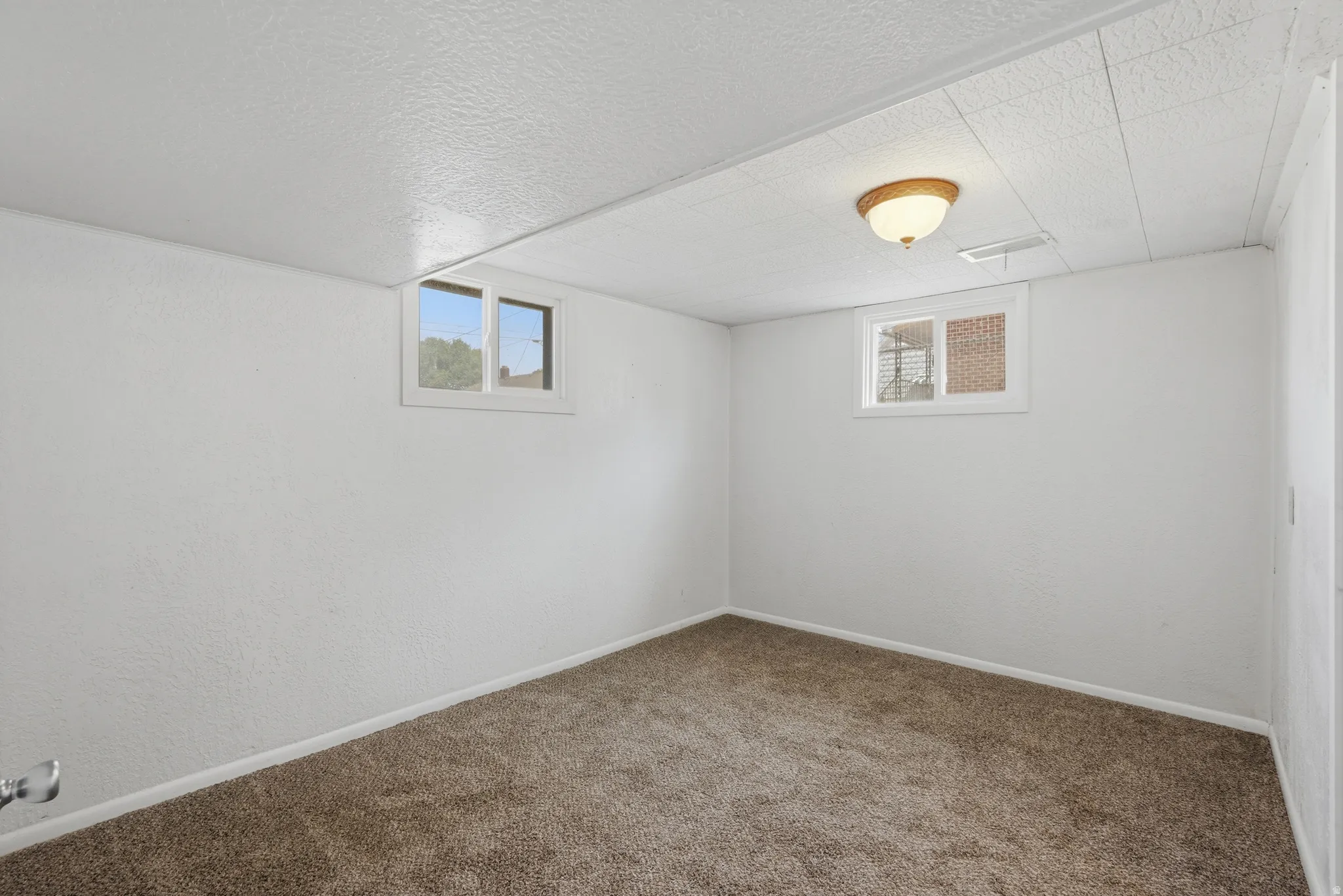 Carpeted room featuring two windows, white walls, and a drop ceiling with an overhead light fixture