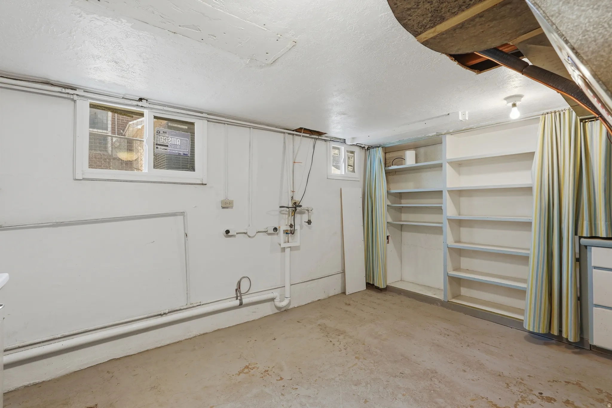 Utility room featuring a concrete floor, built-in shelving, two windows, and exposed ceiling joists