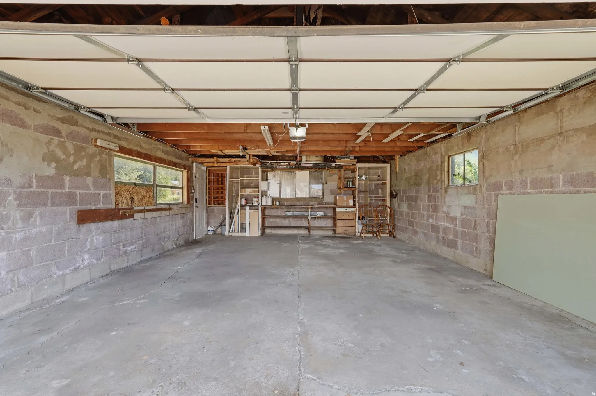 Spacious garage featuring a concrete floor, exposed wood ceiling beams, cinder block walls, and multiple windows providing natural light