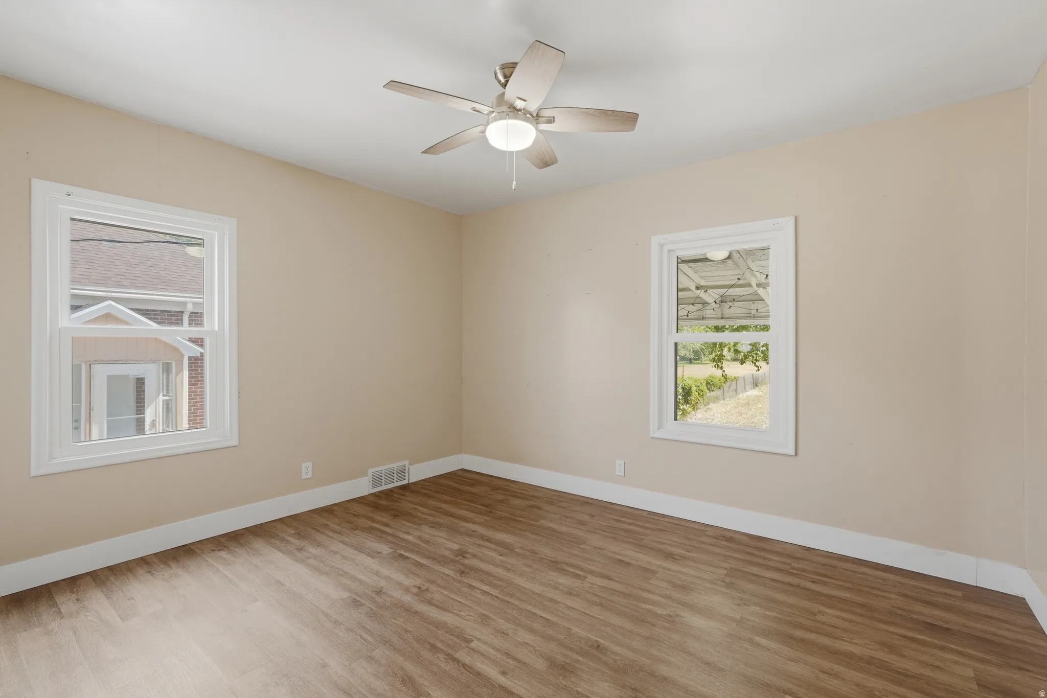 Room featuring wood-finish flooring, neutral wall paint, white baseboards, and two windows with white trim