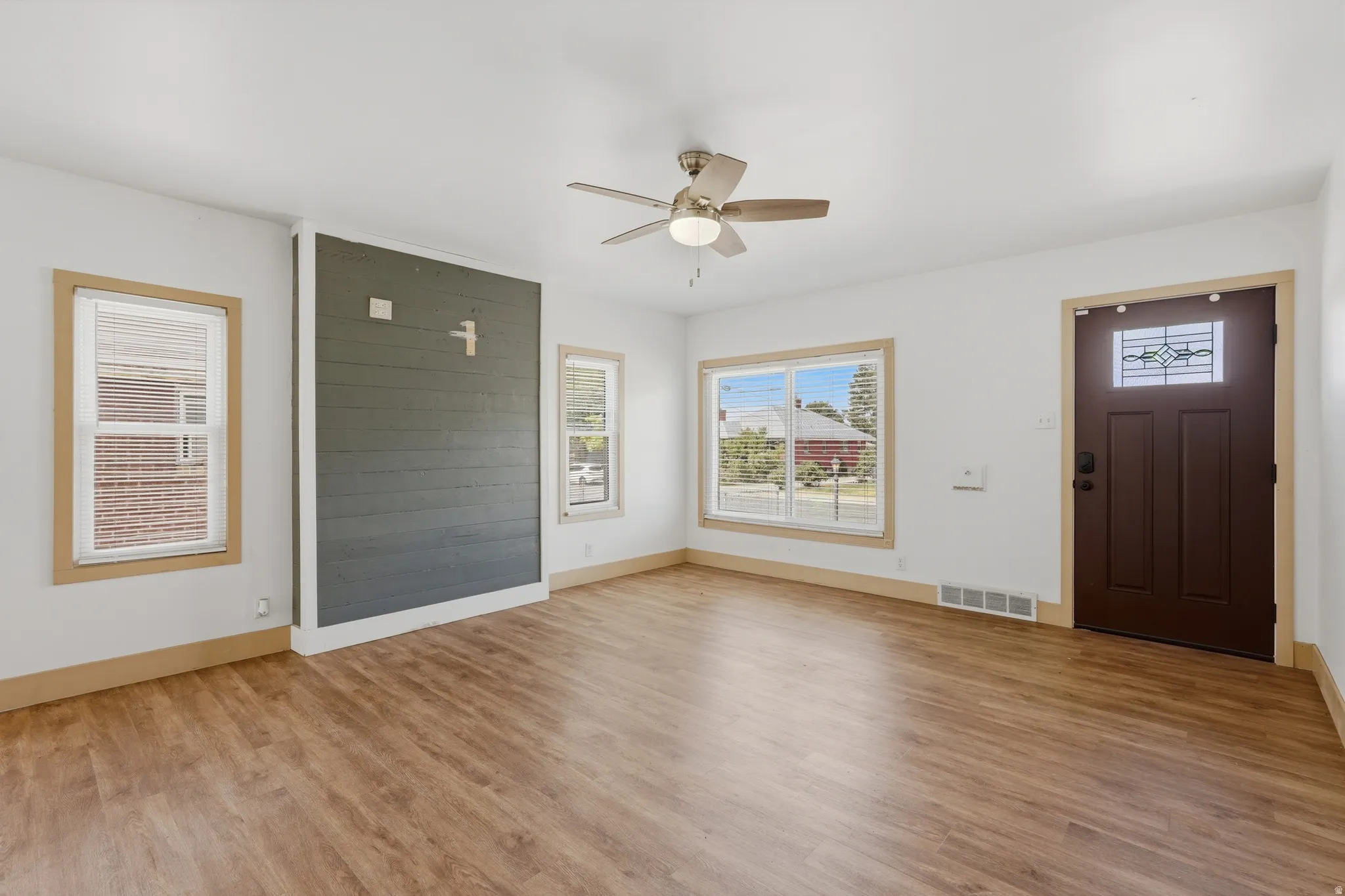 Spacious living area featuring wood-finish flooring, a contemporary ceiling fan, and a prominent accent wall