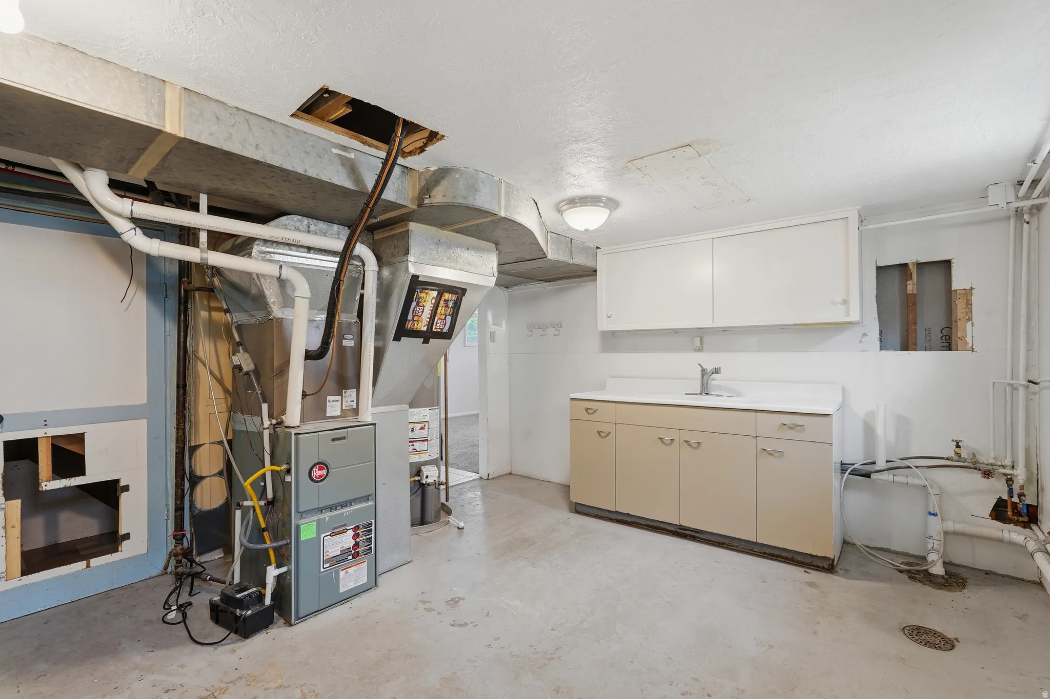 Utility area featuring a furnace system, exposed ductwork, a utility sink with base cabinetry, and overhead wall cabinets