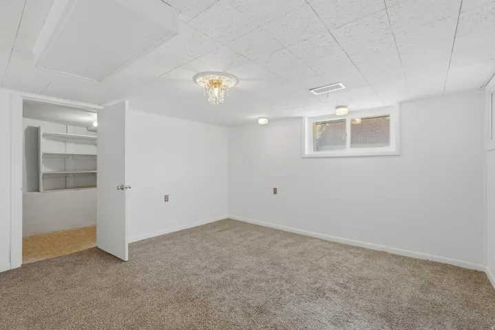Spacious room featuring neutral carpeting, white walls, a drop ceiling, and a prominent window