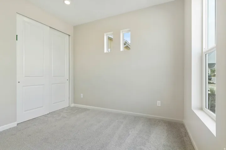 Neutral-toned room featuring light gray carpet, a tall vertical window, two high horizontal windows, a flush-mount ceiling light, and a double bi-fold closet door