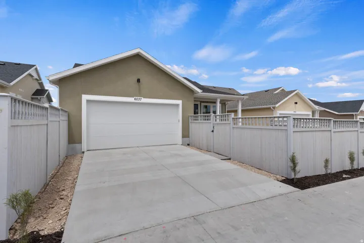 Stucco exterior residence with an attached garage, concrete driveway, and light-toned fencing