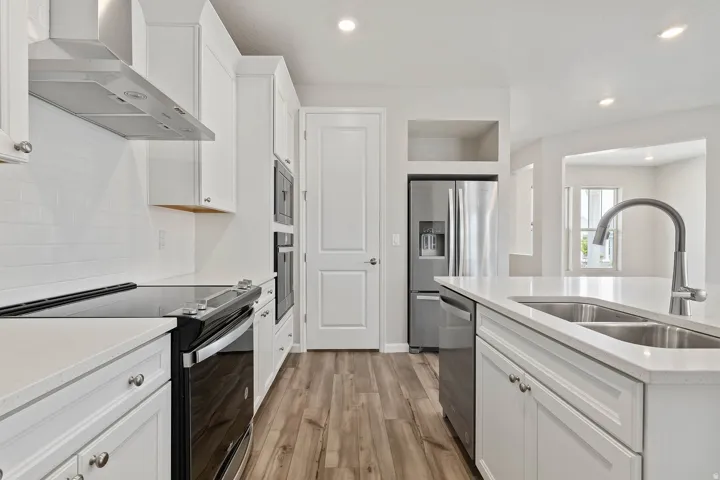 Modern kitchen featuring white cabinetry, stainless steel appliances, wood-finish flooring, recessed lighting, and a white subway tile backsplash