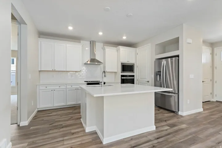 Kitchen featuring a central island with a solid surface countertop, white cabinetry with silver-tone hardware, wood-finish flooring, stainless steel appliances, and a subway tile backsplash