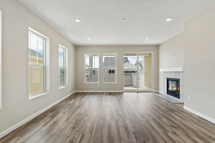 Spacious living area featuring wood-finish flooring, a contemporary fireplace with white tile surround and mantel, multiple windows, recessed ceiling lighting, and a sliding glass door leading to an outdoor patio