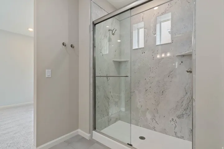 Walk-in shower with clear glass sliding door, light-toned stone-finish tile surround, and integrated shelving