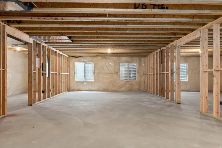 Unfinished basement space featuring exposed wood framing, concrete flooring, and multiple window openings
