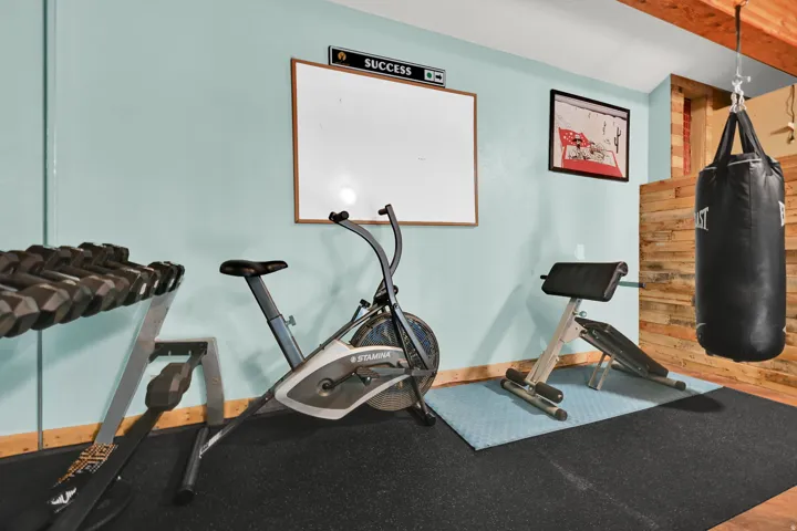 Finished basement space featuring light blue walls, exposed wood ceiling joists, and a wood-paneled accent wall
