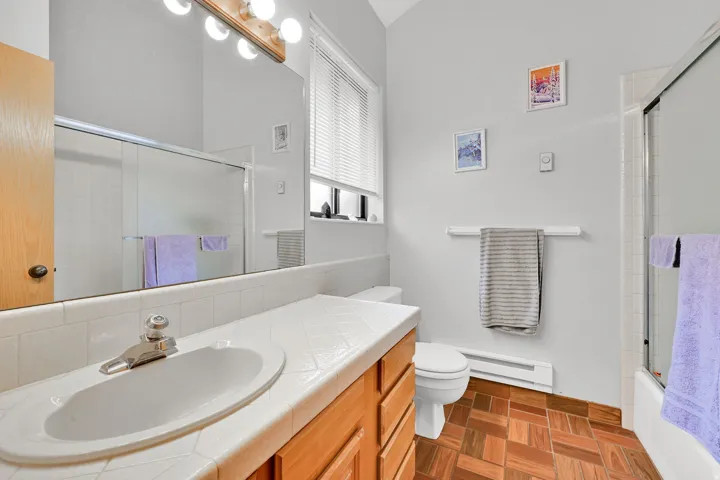 Bathroom featuring a wood-finish vanity with an integrated sink, tile countertop, and a large wall-mounted mirror