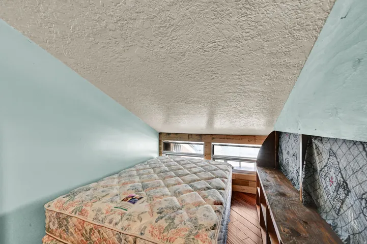 Sloped ceiling space featuring a textured ceiling finish, light blue wall paint, and wood-finish flooring