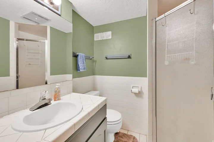 Bathroom featuring a vanity with a drop-in sink, white tiled countertop, large mirror, and a shower with a frosted glass enclosure