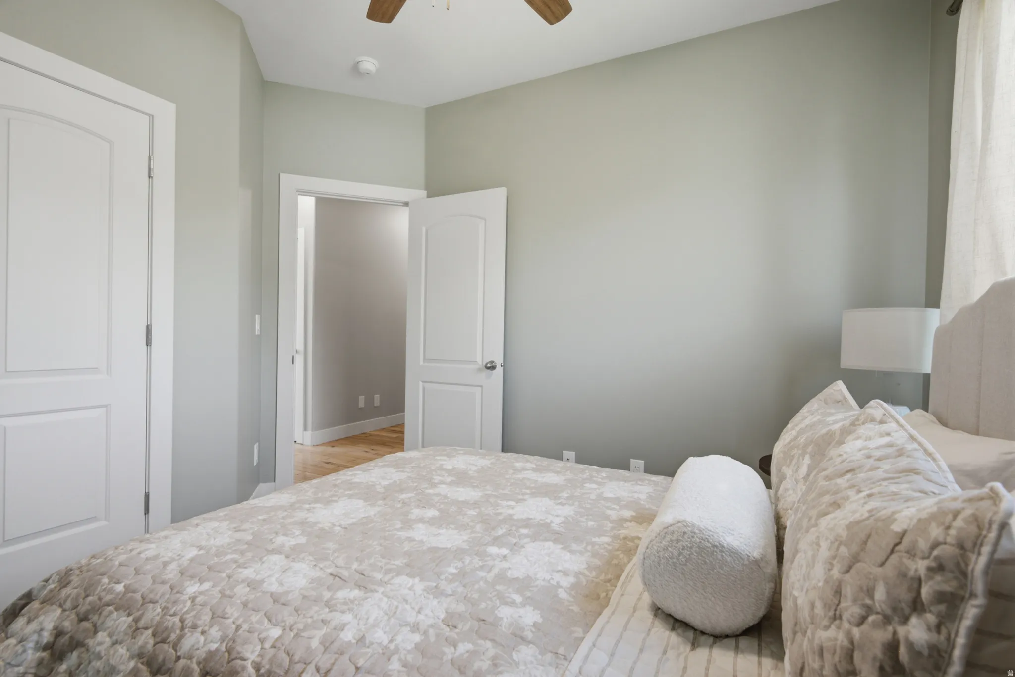 Bedroom featuring light gray wall paint, two white paneled doors, and a ceiling fan with wood-finish blades