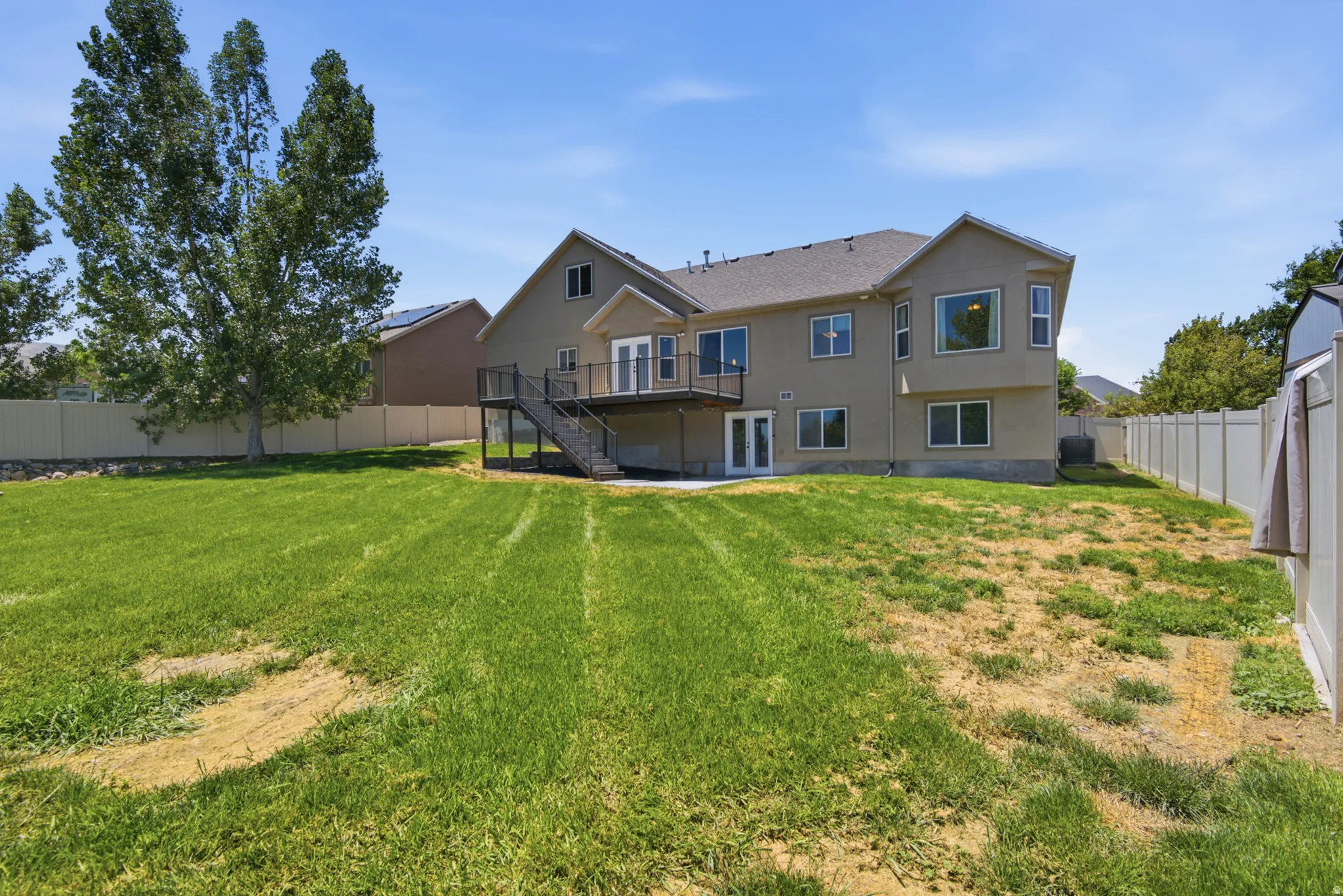 Expansive backyard with a two-story residence featuring a second-level balcony, ground-level patio, multiple windows, and a privacy fence