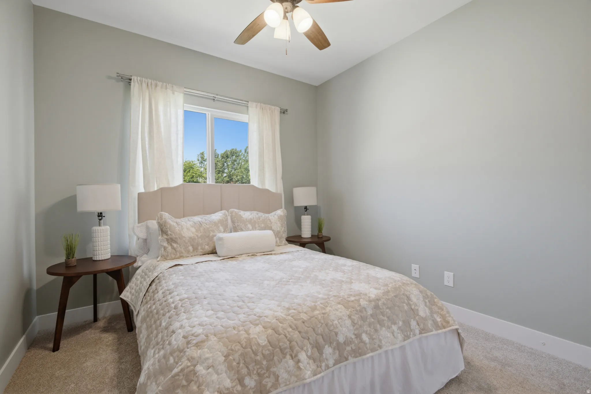 Carpeted room featuring a window with white curtains, light-toned walls, and a ceiling fan with integrated lighting