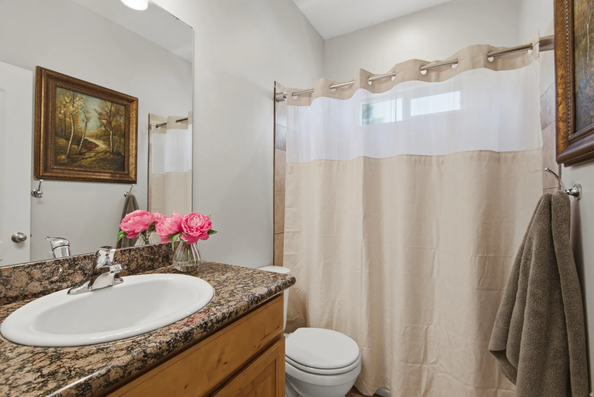 Bathroom featuring a granite-finish countertop with an undermount sink, chrome faucet, wood-finish vanity, and a shower with tile surround