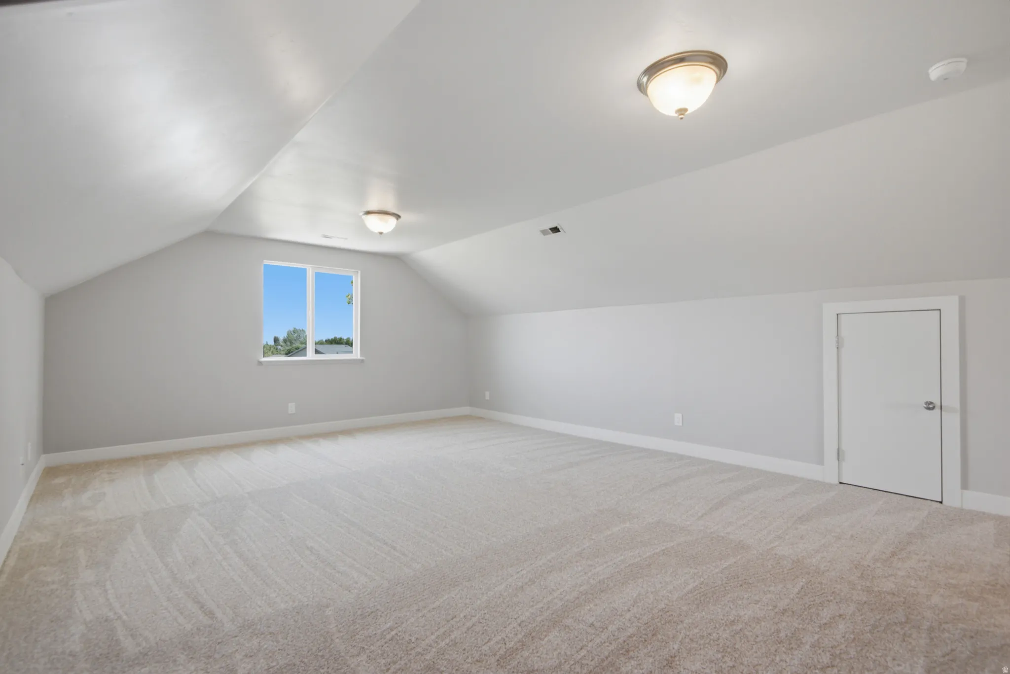 Spacious attic room featuring sloped ceilings, light carpeting, and neutral wall tones