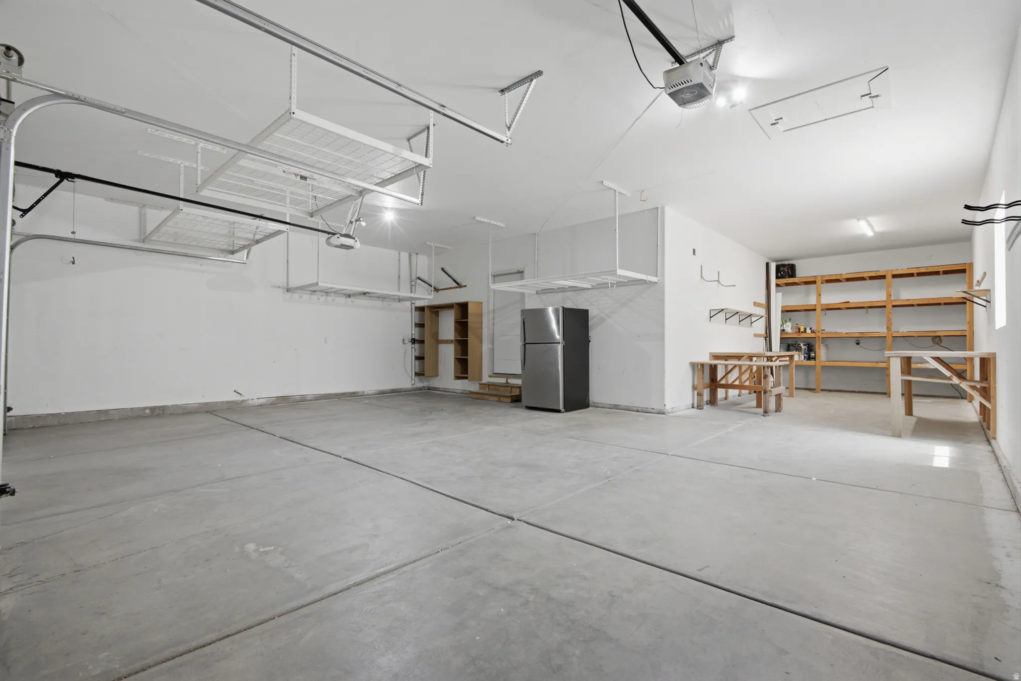 Spacious garage featuring a concrete floor, overhead storage racks, exposed shelving, built-in wooden cabinetry, and bright overhead lighting