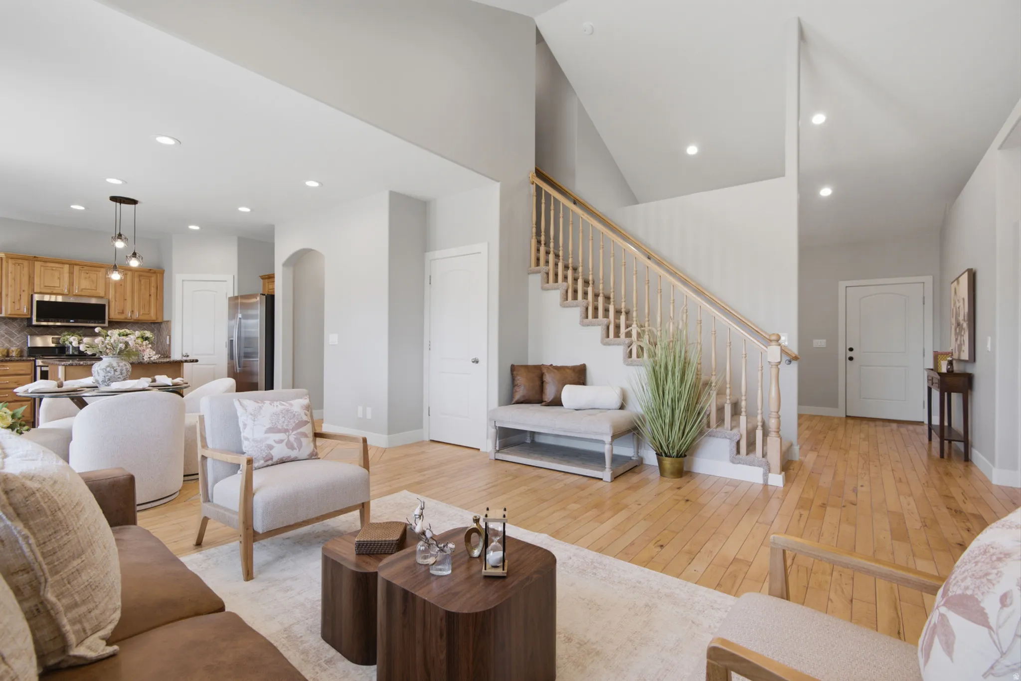 Expansive living area featuring light wood-finish flooring throughout, a grand staircase with wood railing, recessed lighting, and vaulted ceilings