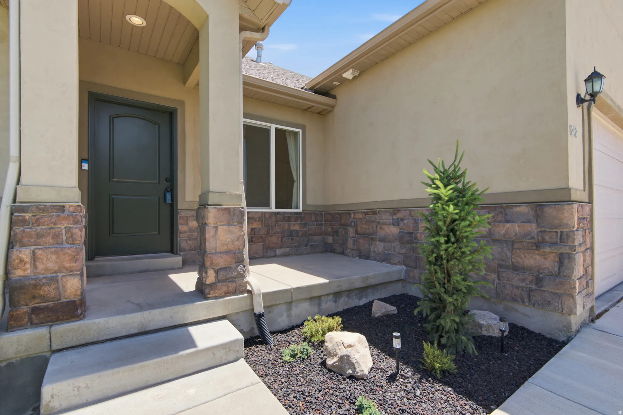 Entryway featuring a dark green paneled door, stone veneer accents, stucco exterior, covered porch, and concrete steps