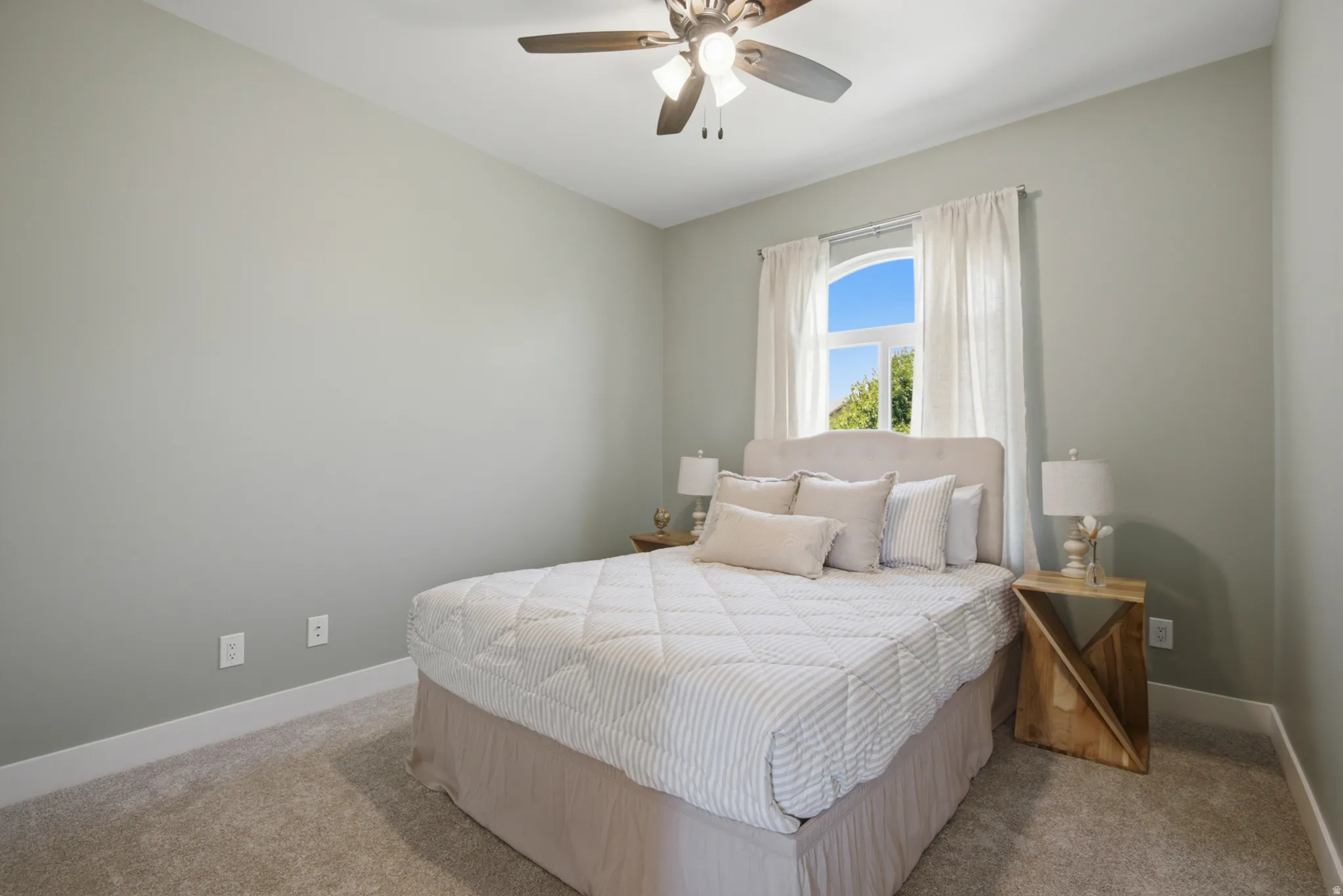 Carpeted room featuring a ceiling fan, arched window, and light gray walls with white baseboards