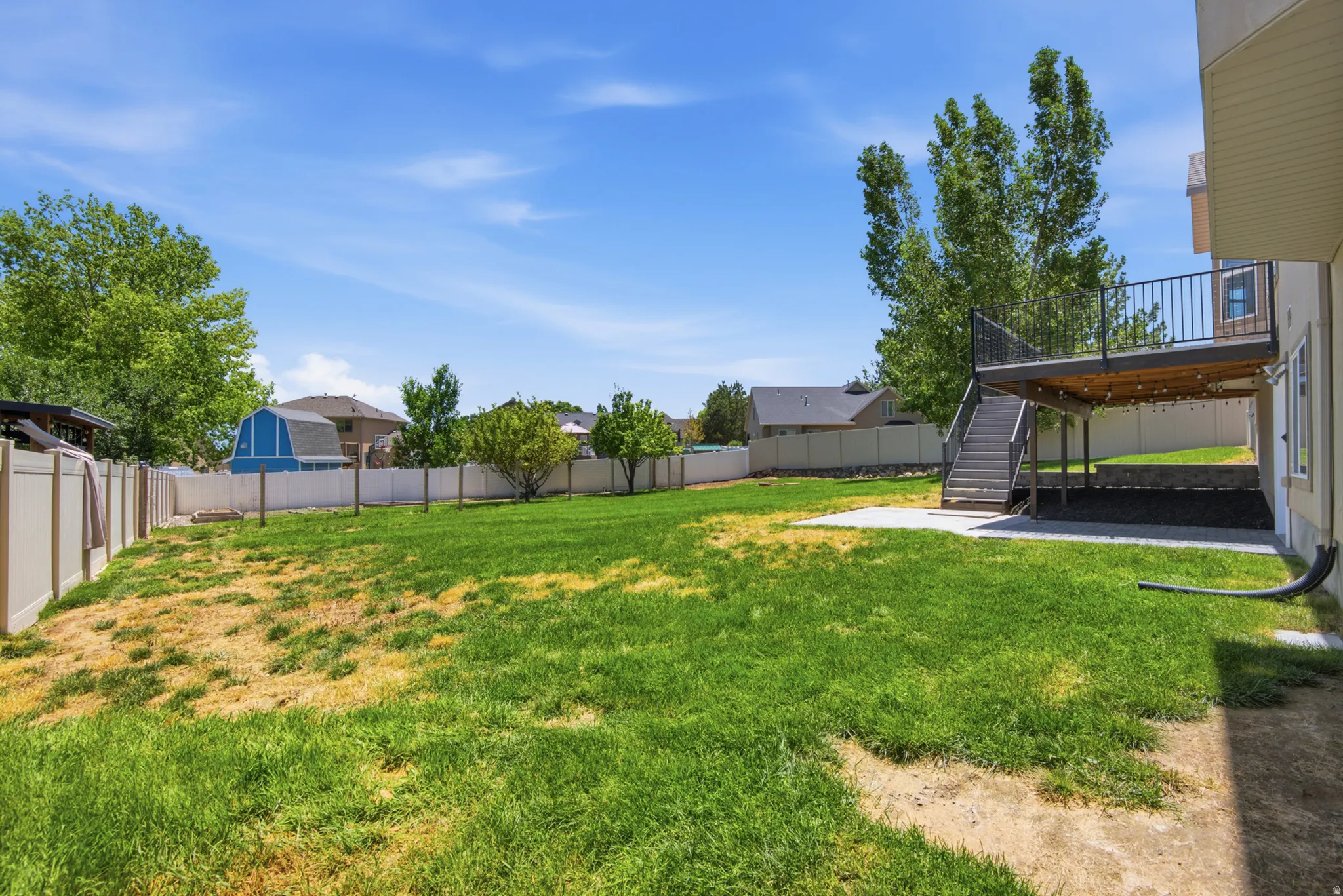Expansive rear yard featuring a large lawn area, a multi-level deck with black railings, and a concrete patio