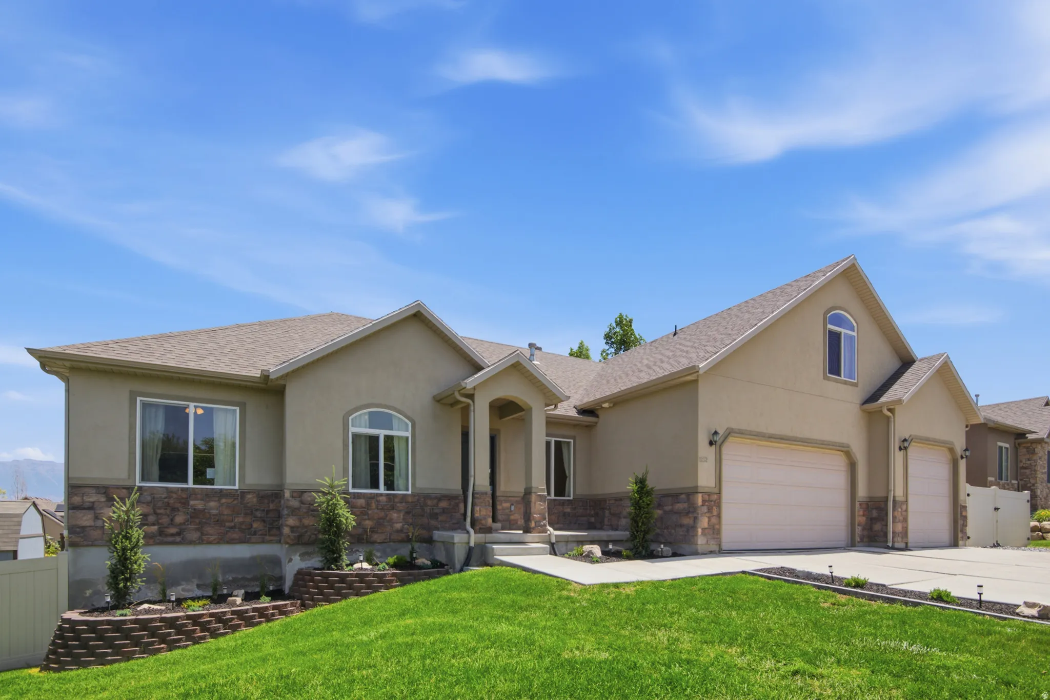 Contemporary stucco home with a stone facade, featuring a multi-car garage, arched entry, and established landscaping