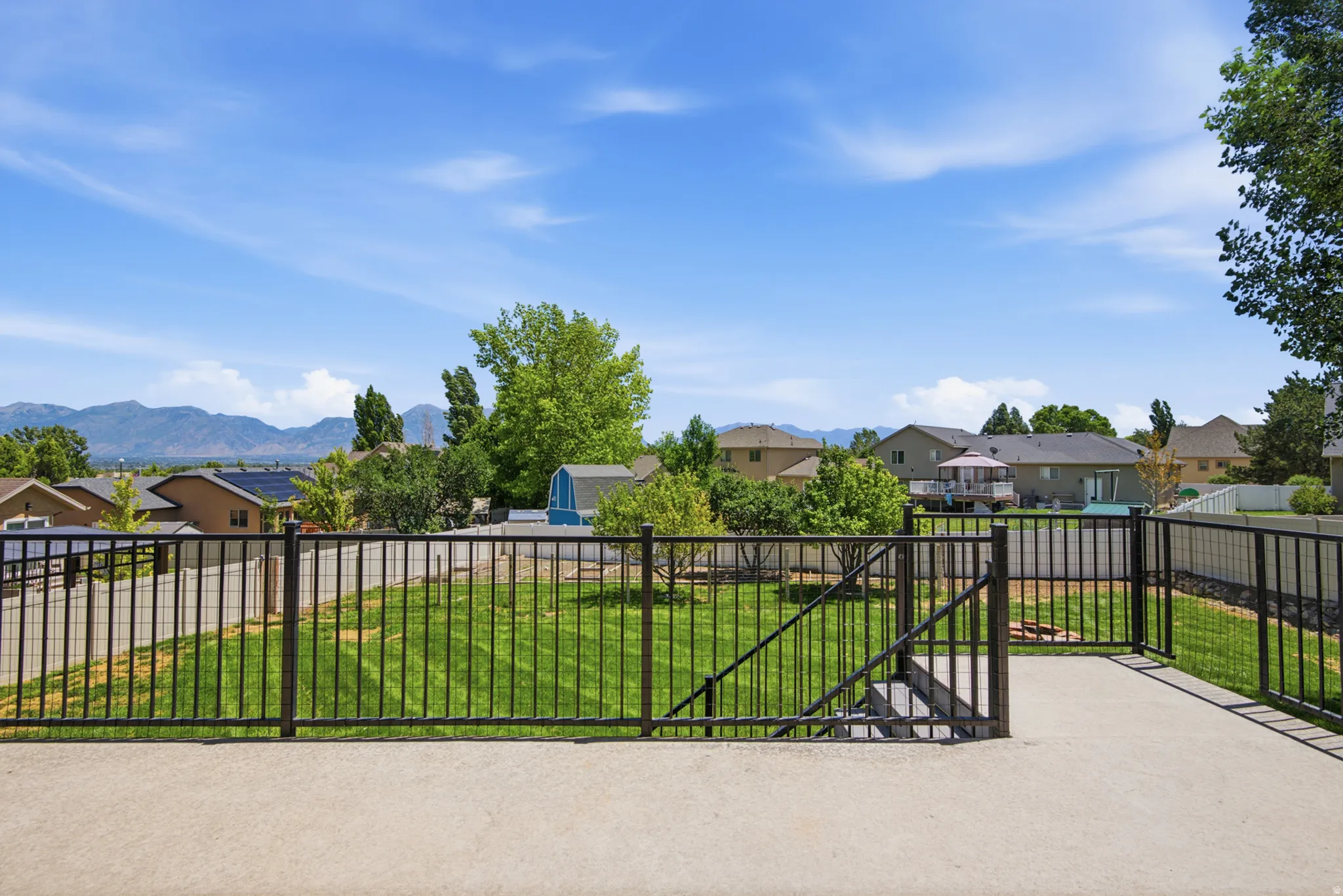 Concrete patio with a black metal fence and gate overlooking a grassy yard
