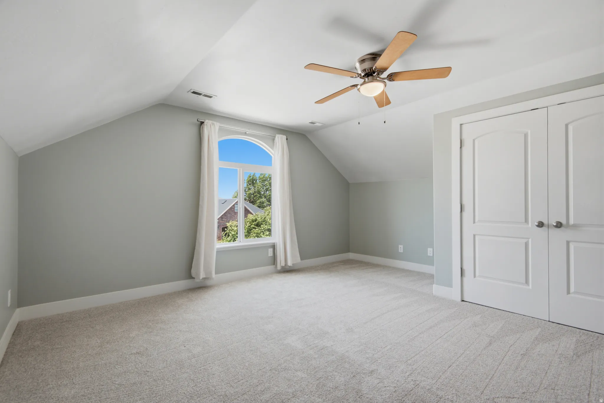 Spacious room featuring vaulted ceilings, light gray wall paint, and plush carpeting