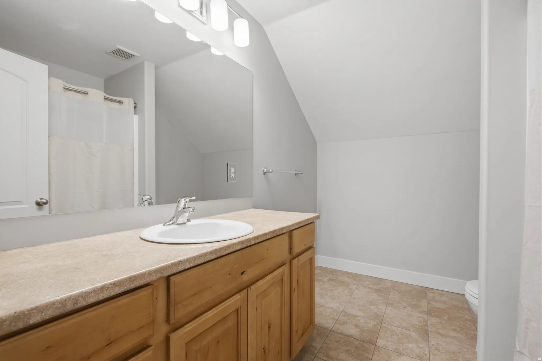 Light wood-finish vanity cabinetry with an integrated countertop, undermount sink, and polished chrome faucet