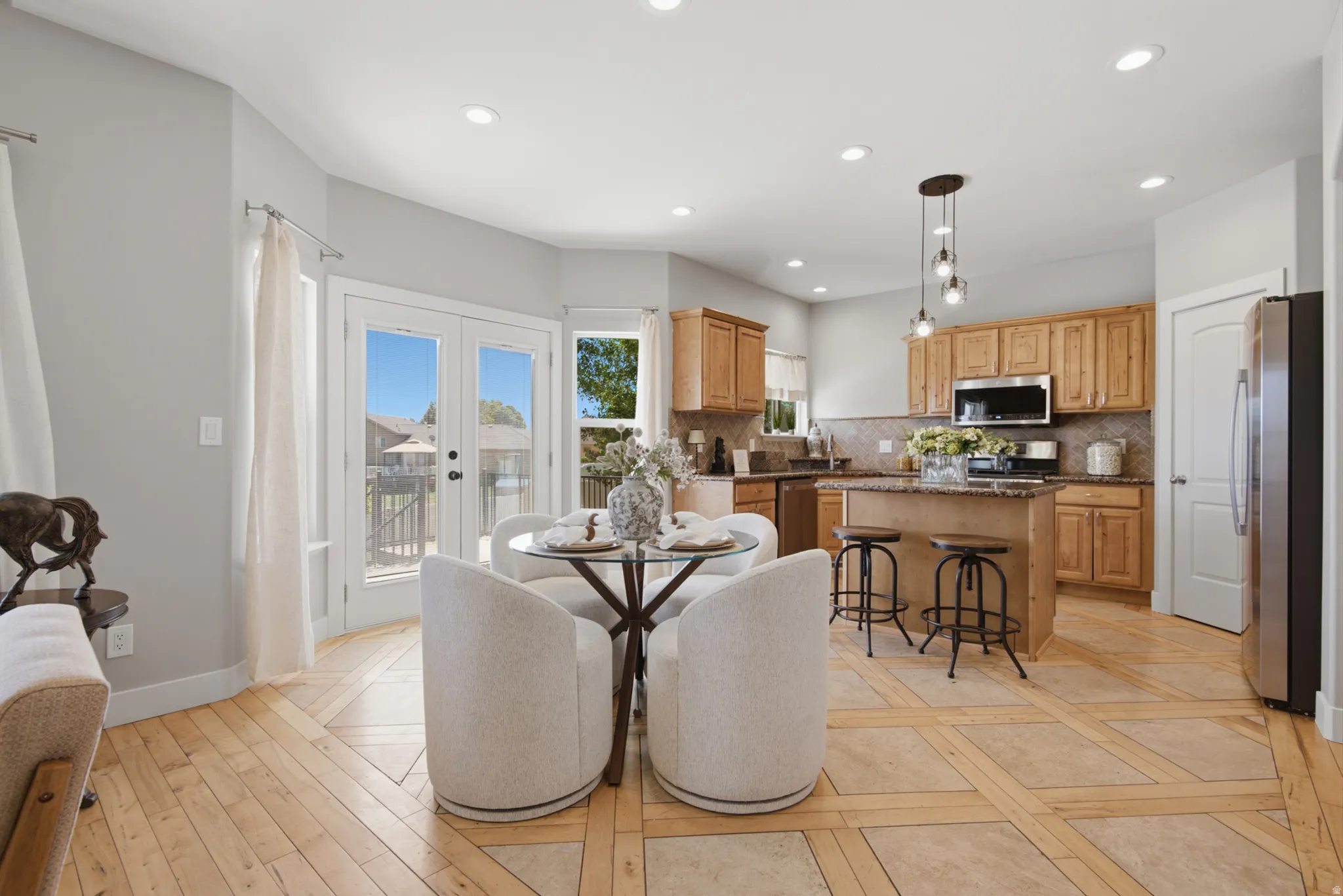 Open-concept kitchen and dining area featuring light wood-finish flooring with tile accents, stainless steel appliances, a central island with a granite-style countertop, and recessed lighting